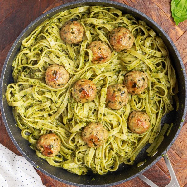 Easy basil pesto pasta with meatballs all mixed together in a large skillet.