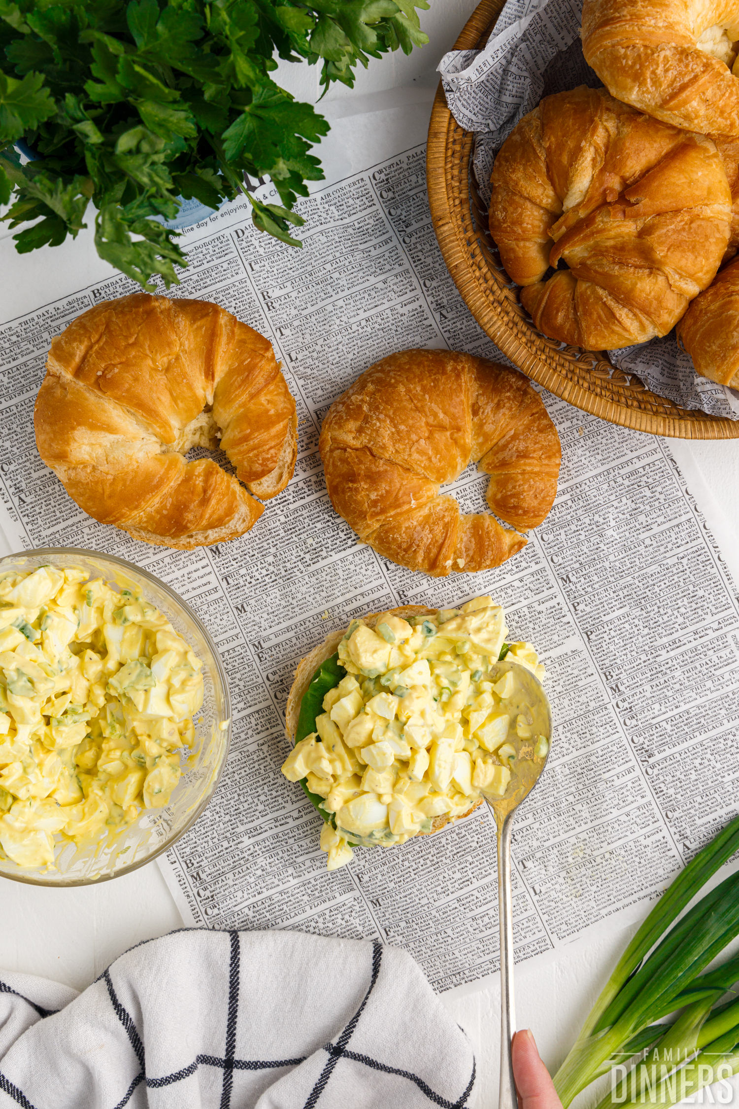 Croissants cut open with egg salad mixture being spooned on top.