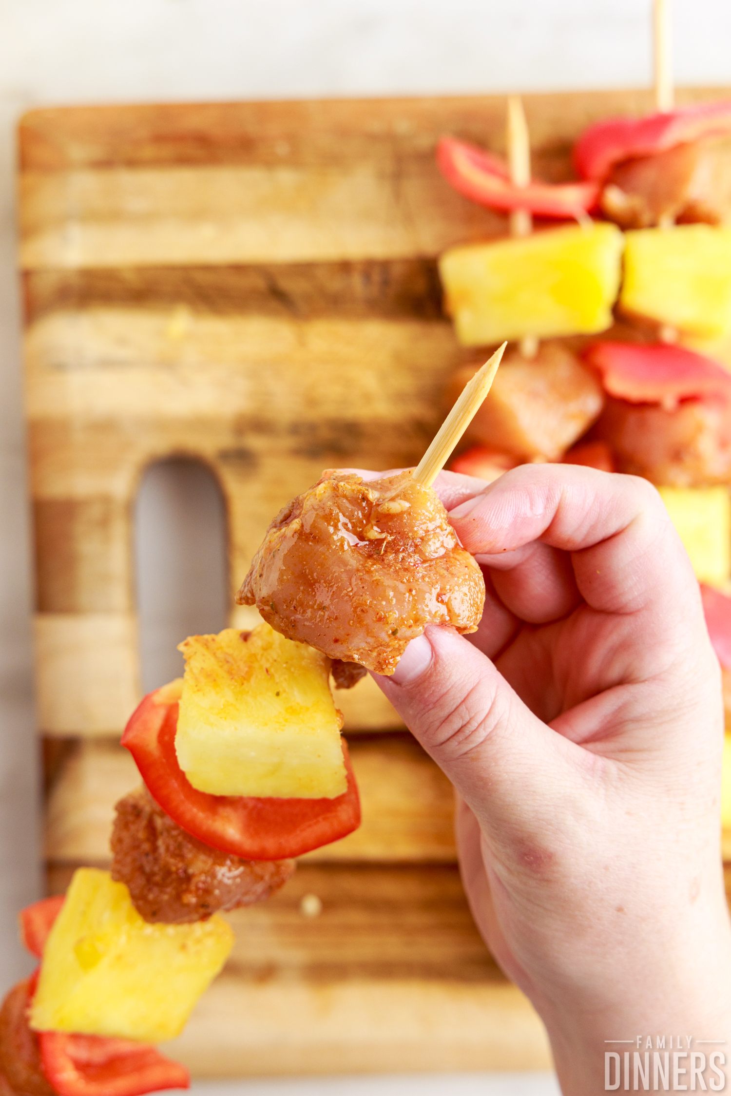 chicken being put on a skewer of pineapple and red pepper
