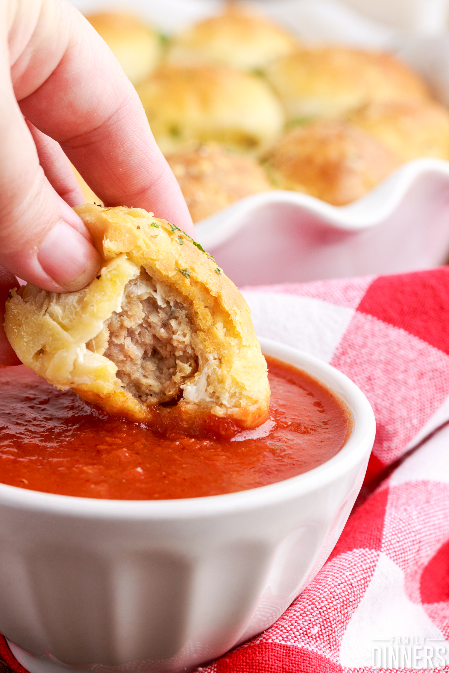 mozzarella meatball bomb with a bite taken out being dipped into marinara sauce