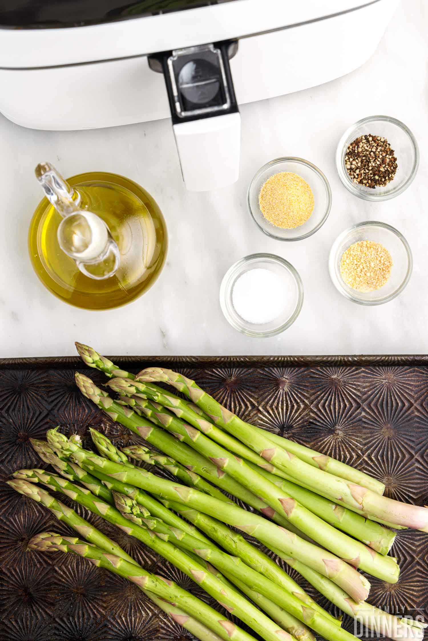 Ingredients for making air fryer asparagus on the counter, including oil, salt and pepper, and onion and garlic powder.