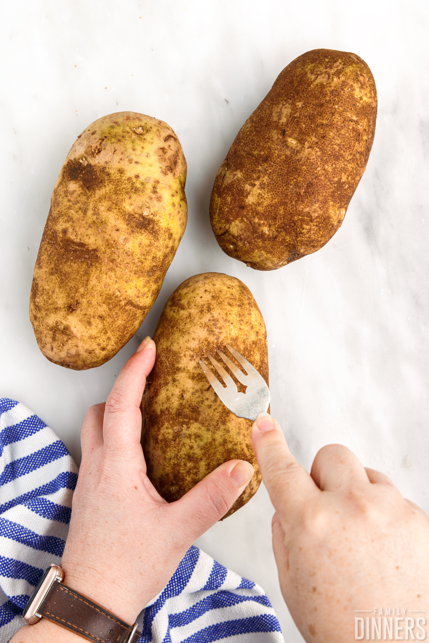 3 clean, raw potatoes being pierced by a fork.