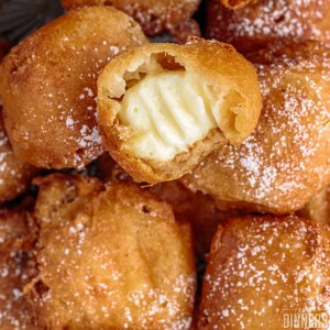 pile of deep fried cheesecake, the top one has a bite take out to expose the filling