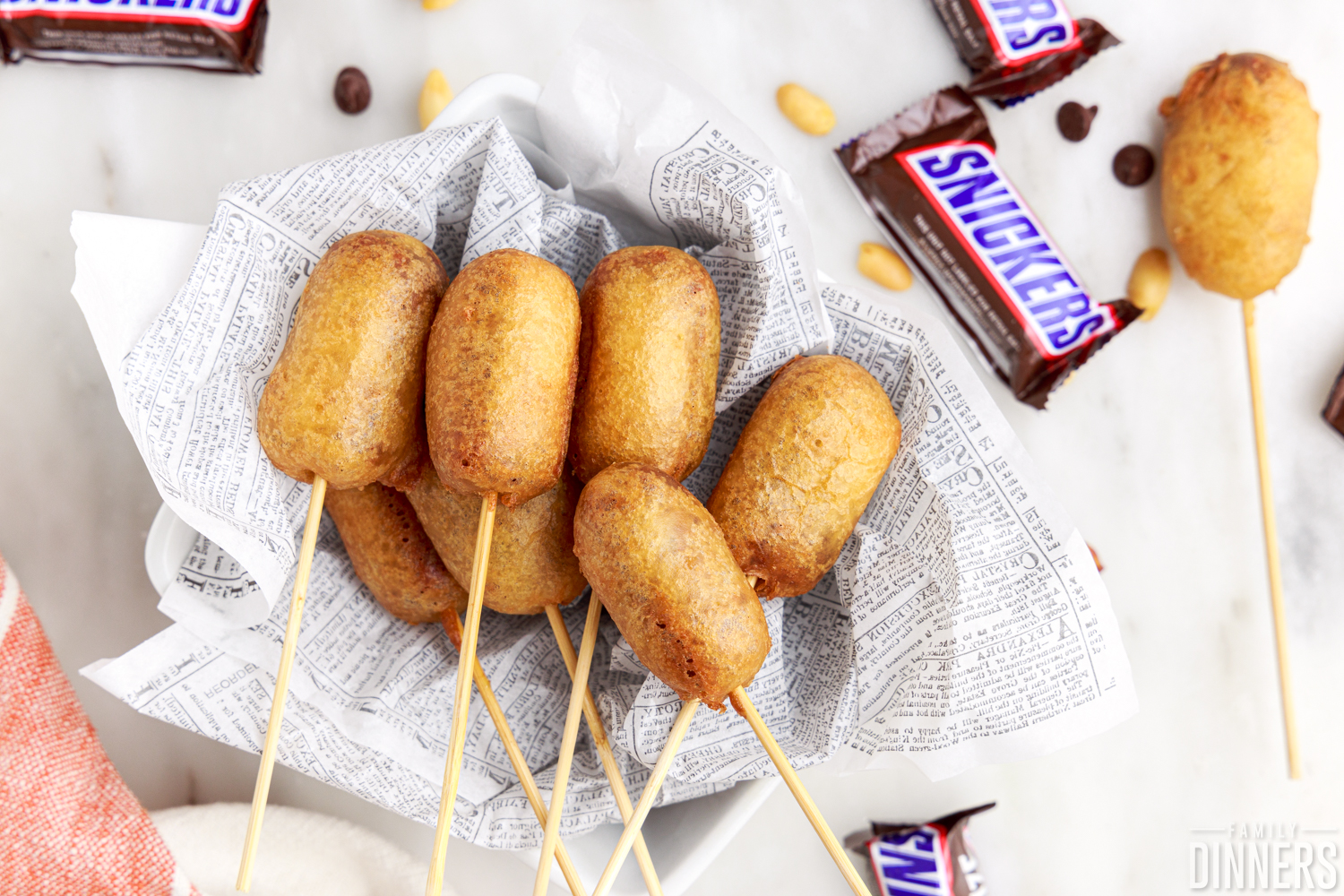 pile of deep fried snickers on a piece of paper, one deep fried snickers sitting on the counter nest to them, some fun-sized snickers bars scattered around them