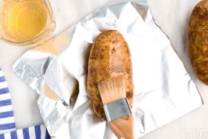 brushing oil on baked potato sitting on foil