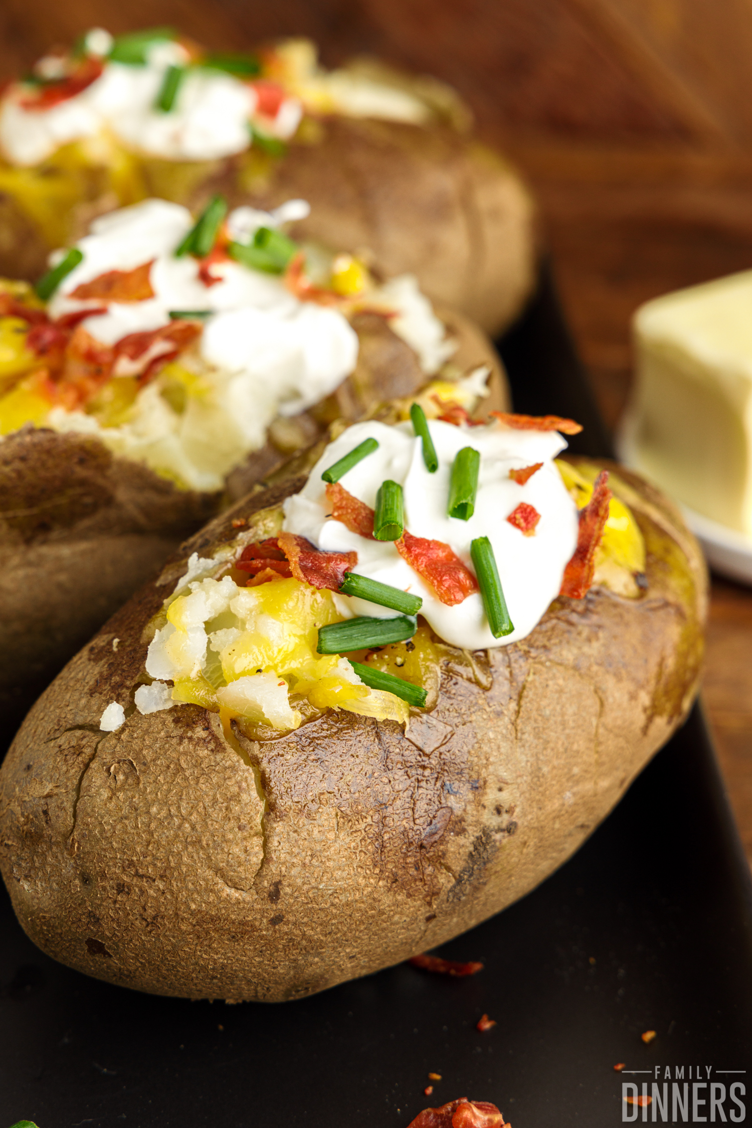 Close up of baked potatoes cut open and loaded with cheese, sour cream, chives and bacon bits.