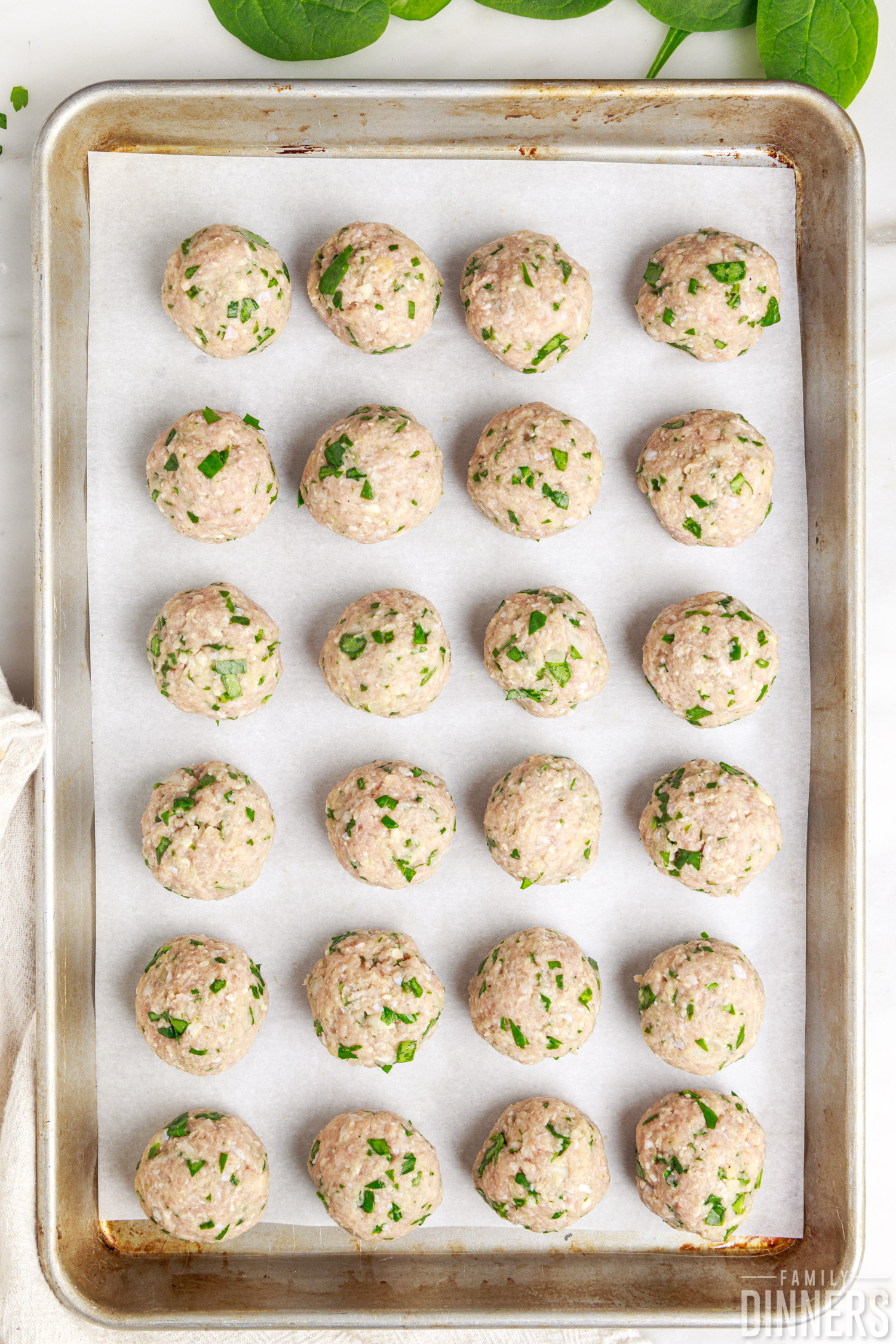 baking sheet with parchment paper and six rows of four meatballs, uncooked