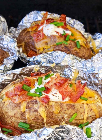 Loaded baked potato in foil on a grill.