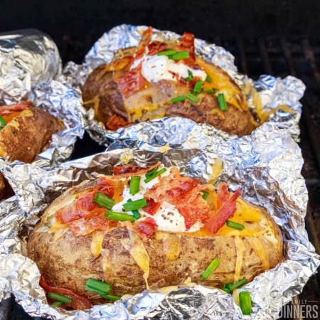 Loaded baked potato in foil on a grill.