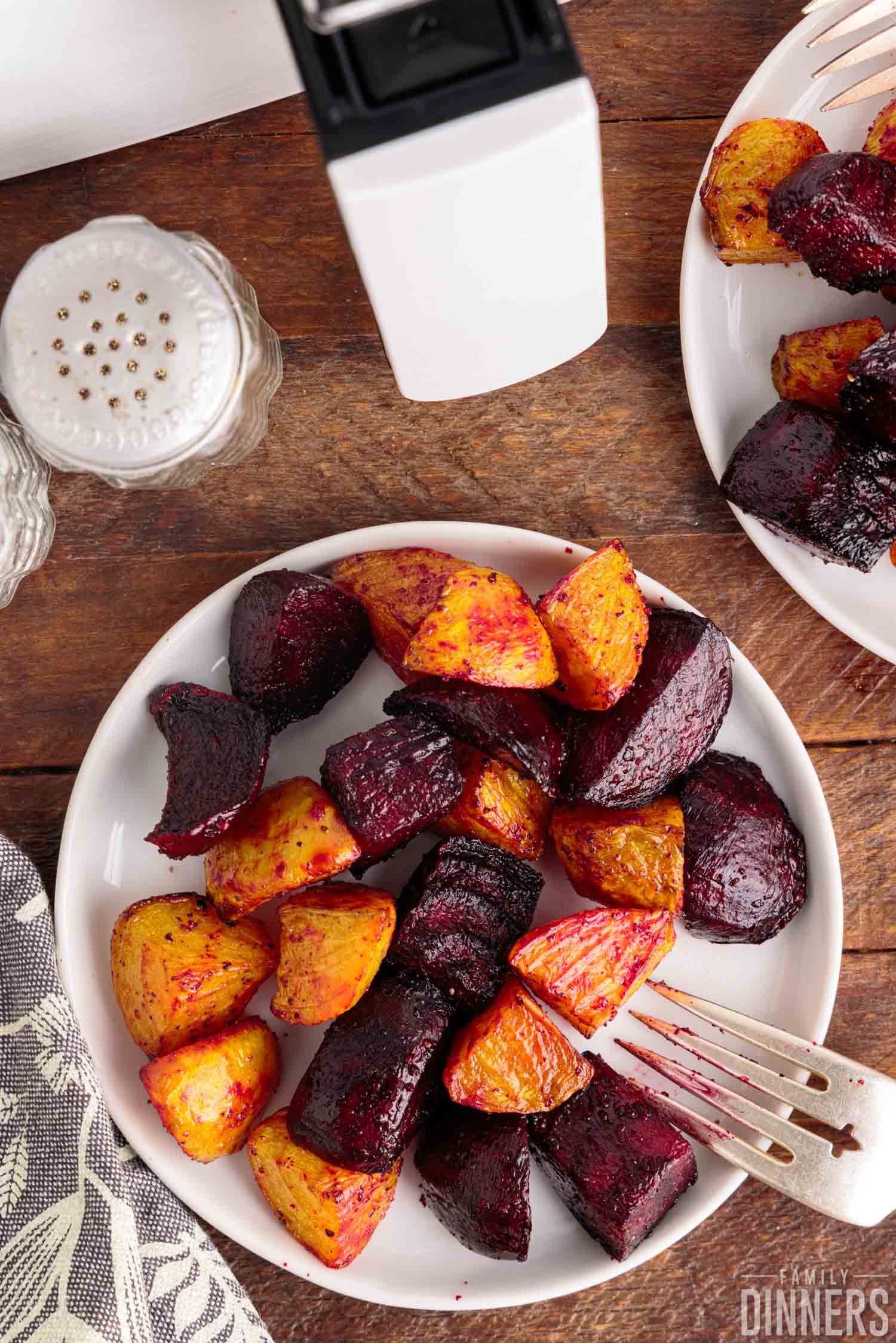 Air fryer beets on a round, white plate with a fork on a wooden board with a salt shaker