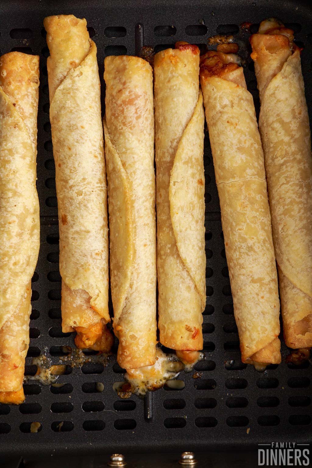 cooked taquitos in an air fryer basket.