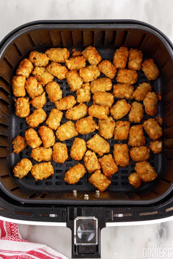 cooked tater tots in air fryer basket.