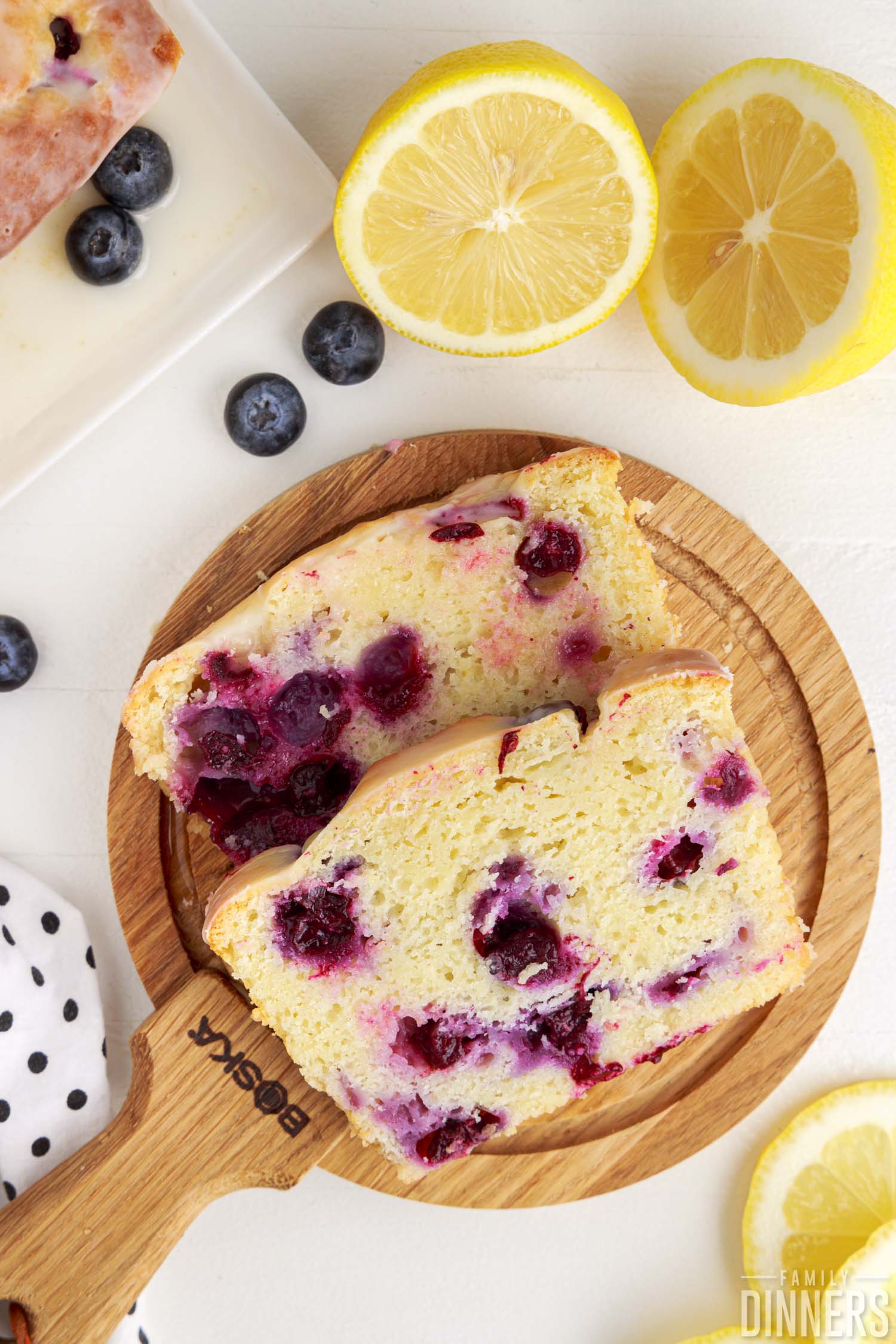 A slice of lemon blueberry bread on a cutting board next to a sliced lemon and some blueberries.