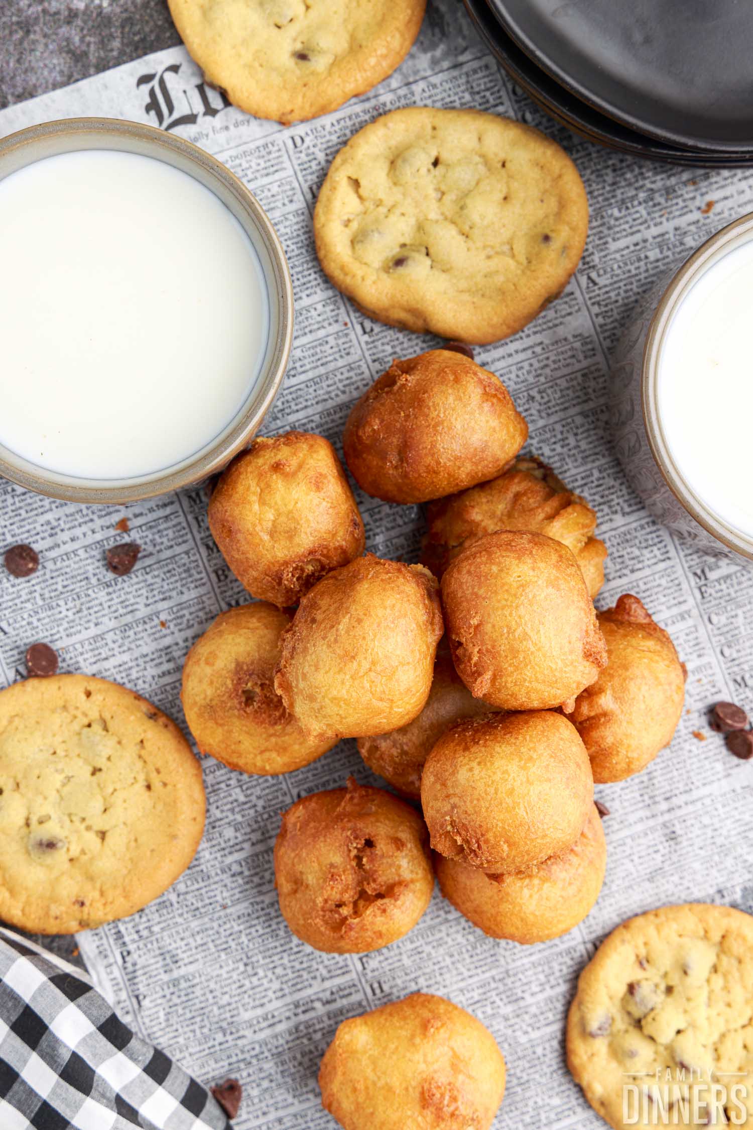pile of deep fried cookie dough bites on a paper, with baked cookies and cups of milk