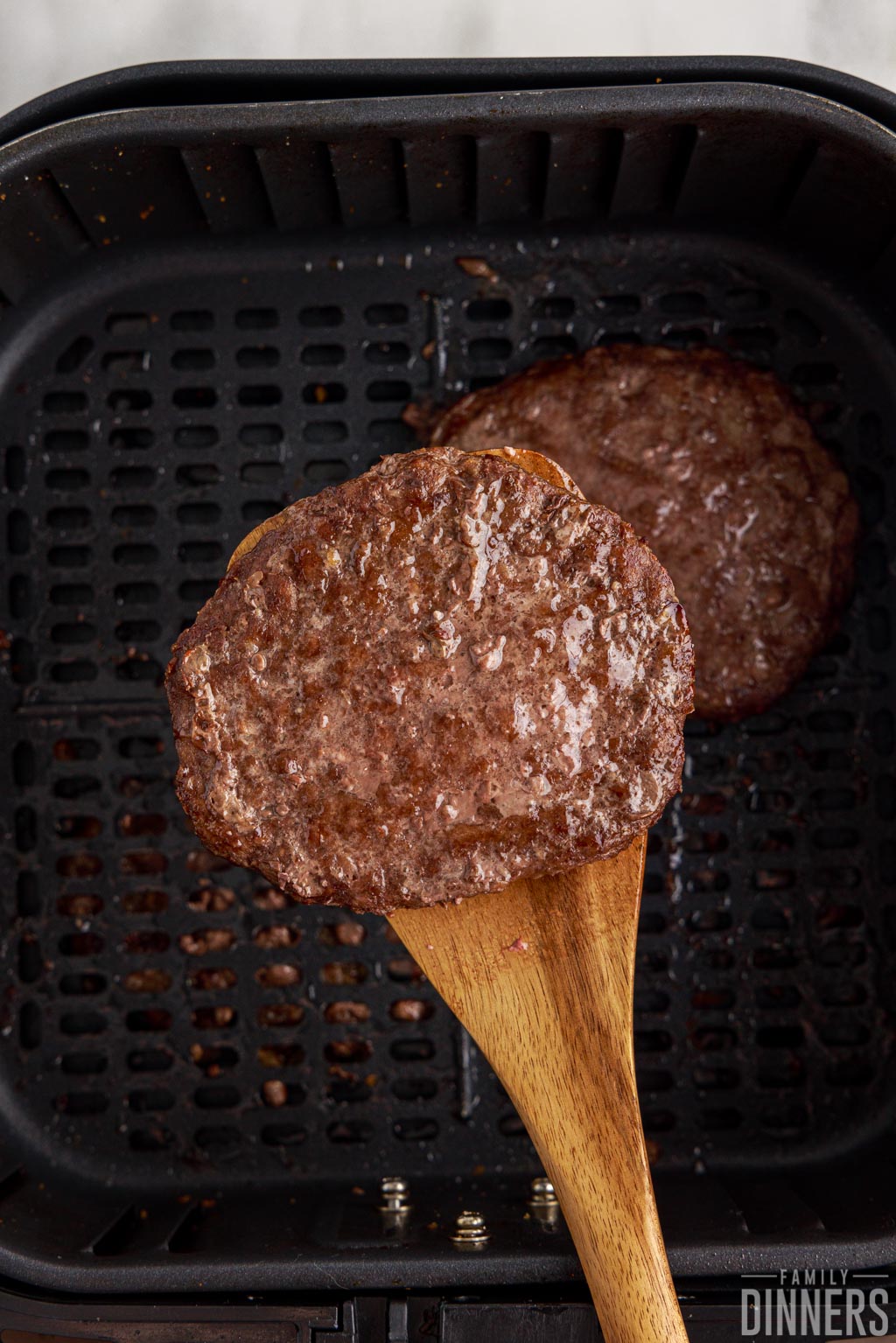 Cooked hamburger patty on a spatula over an air fryer basket.