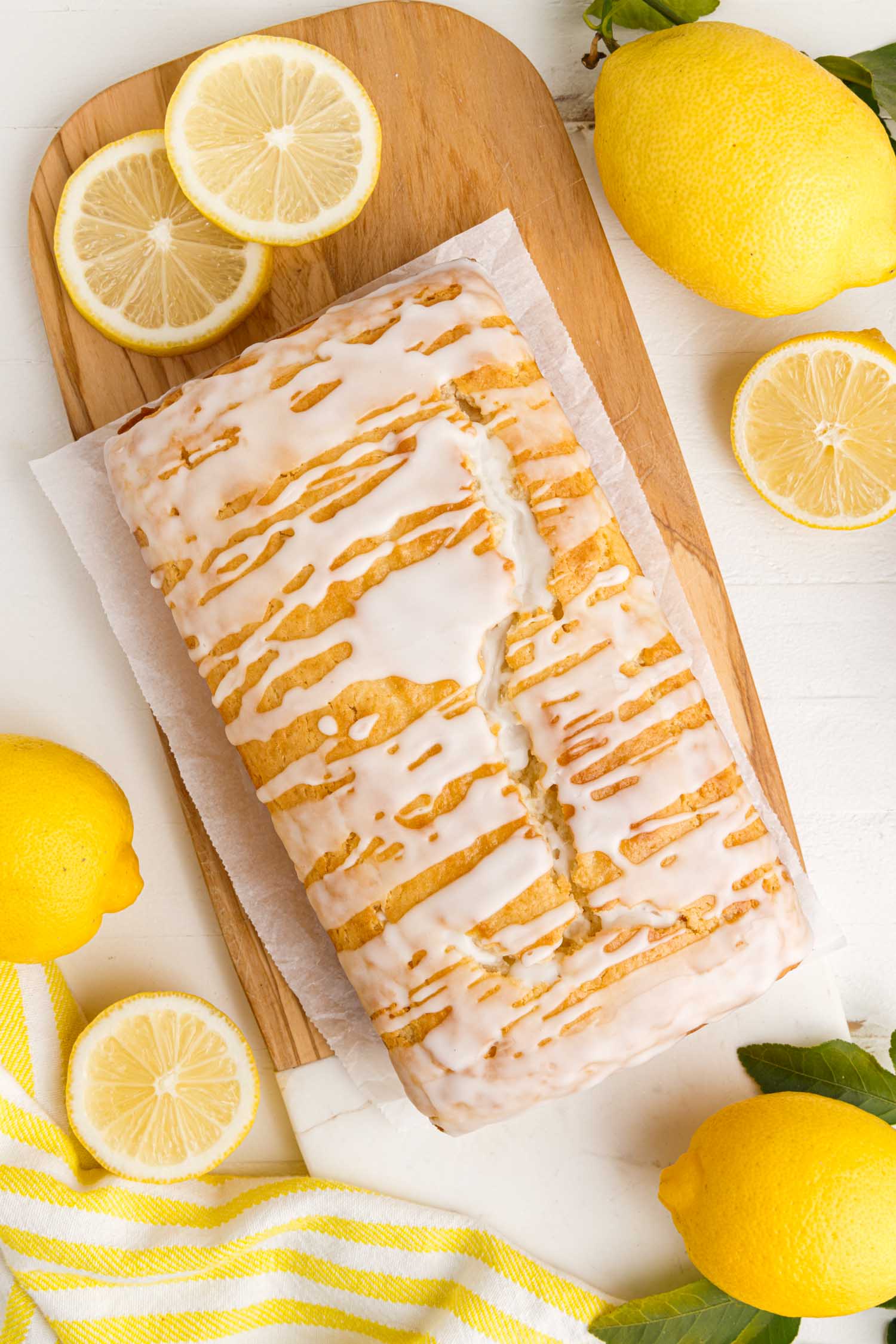glazed lemon bread loaf on a wooden board with whole and cut lemons around it