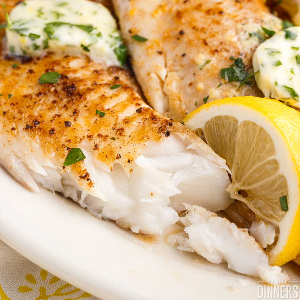 tilapia on a plate with lemon butter and lemon slices
