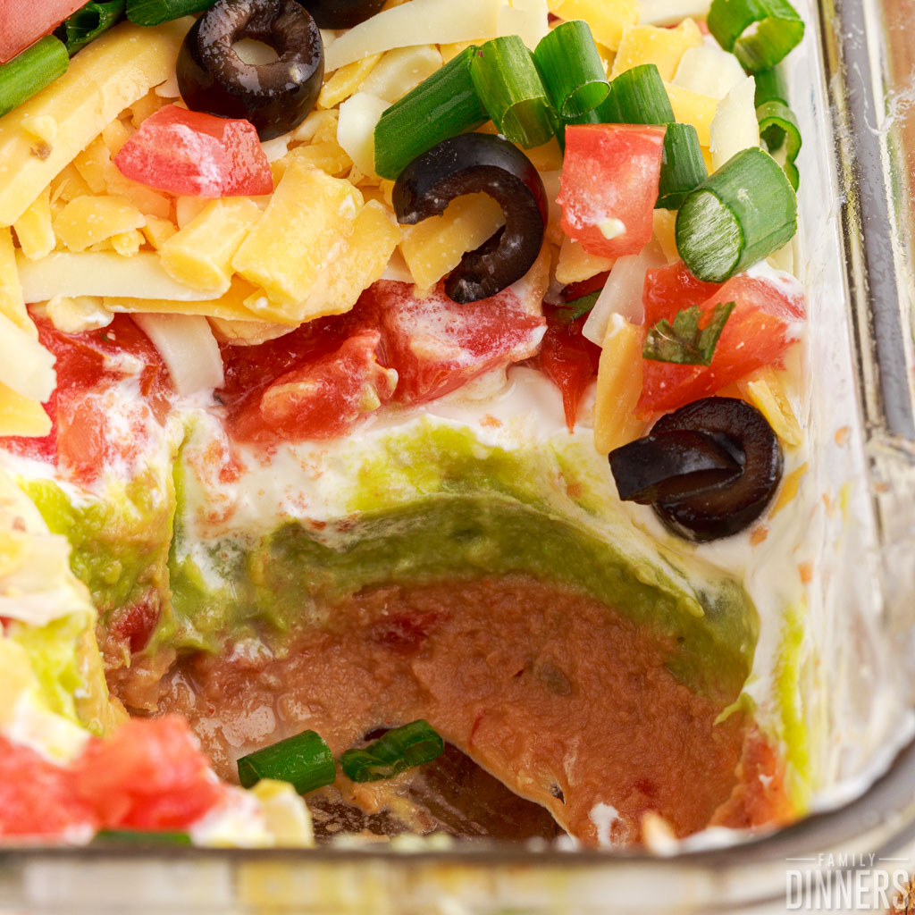 Easy 7 layer bean dip in a glass dish with some taken out of it