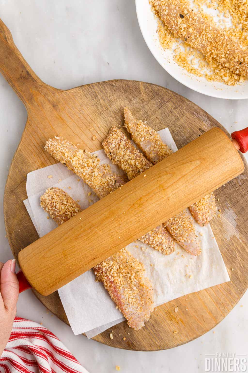 pushing bread crumbs on fish with rolling pin