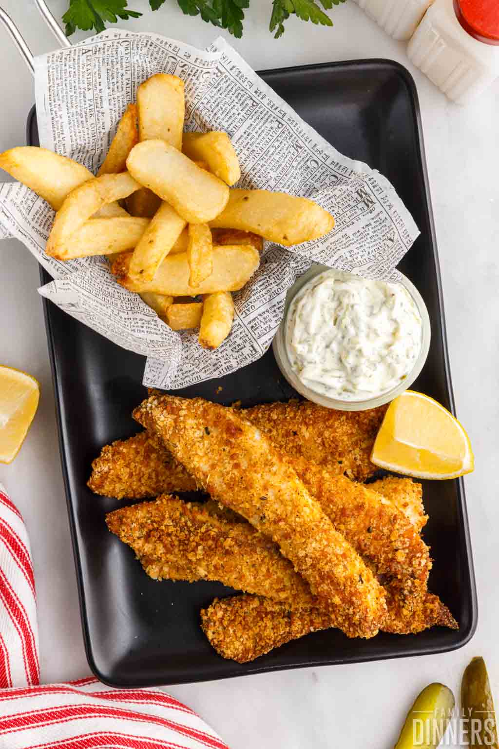 fried fish with fries and tartar sauce on a black plate