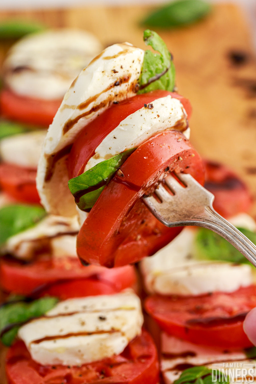 Caprese salad (tomato and mozzarella nd basil with oil and vinegar stacked on a fork.