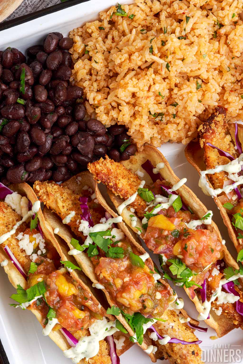 Fried fish tacos on a plate with rice and beans.