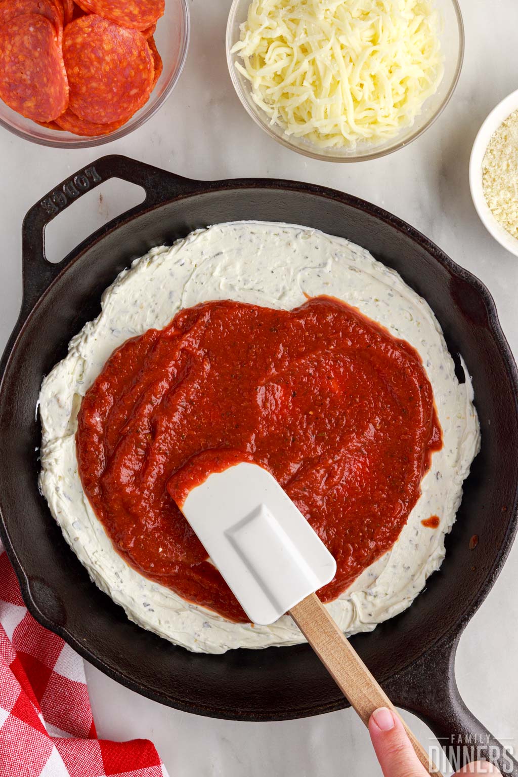 Pizza sauce being spread over cheese mixture in a cast iron pan.