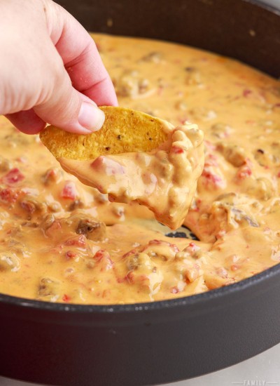 Hand dipping a chip into the rotel dip in a frying pan.
