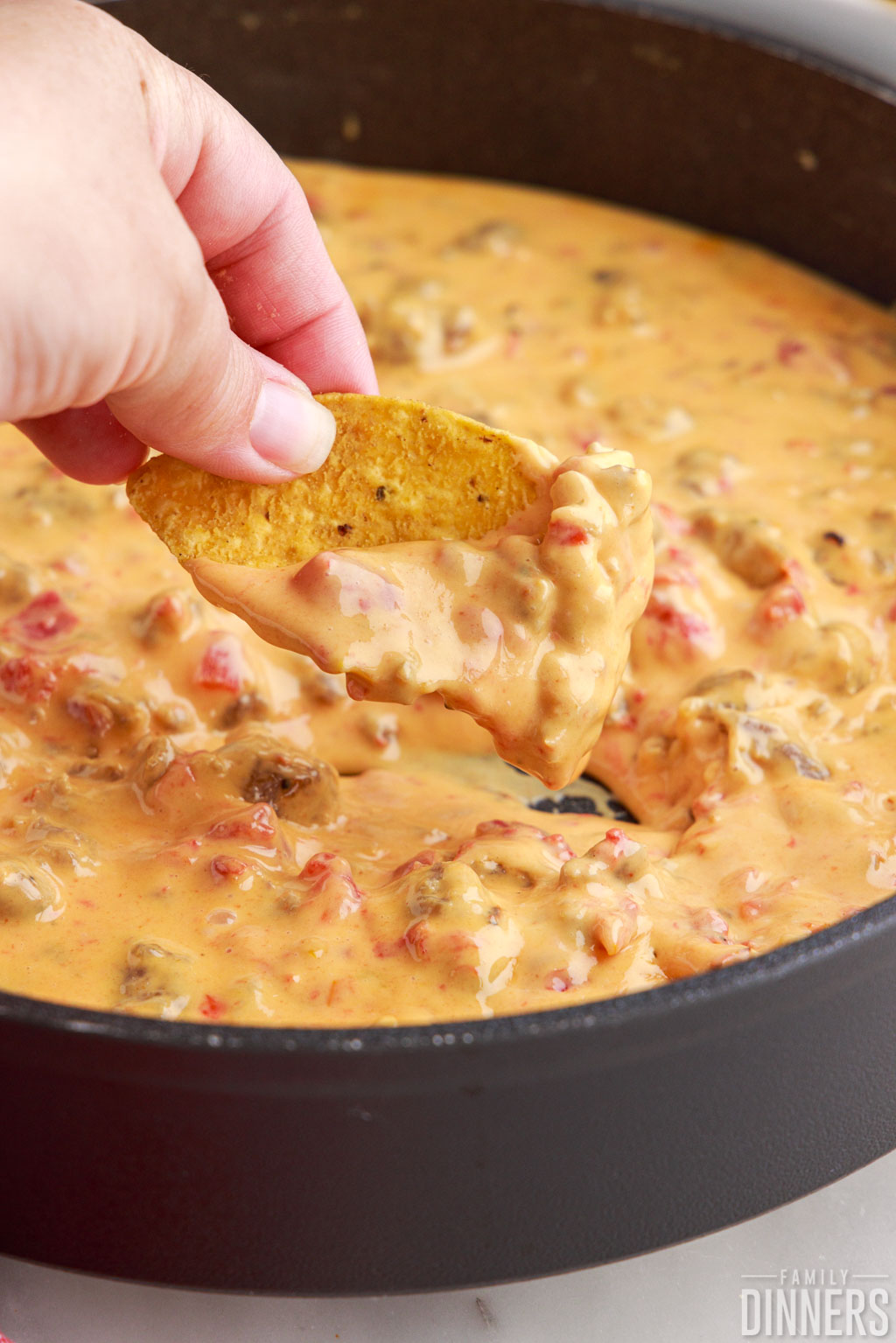 Hand dipping a chip into the rotel dip in a frying pan.