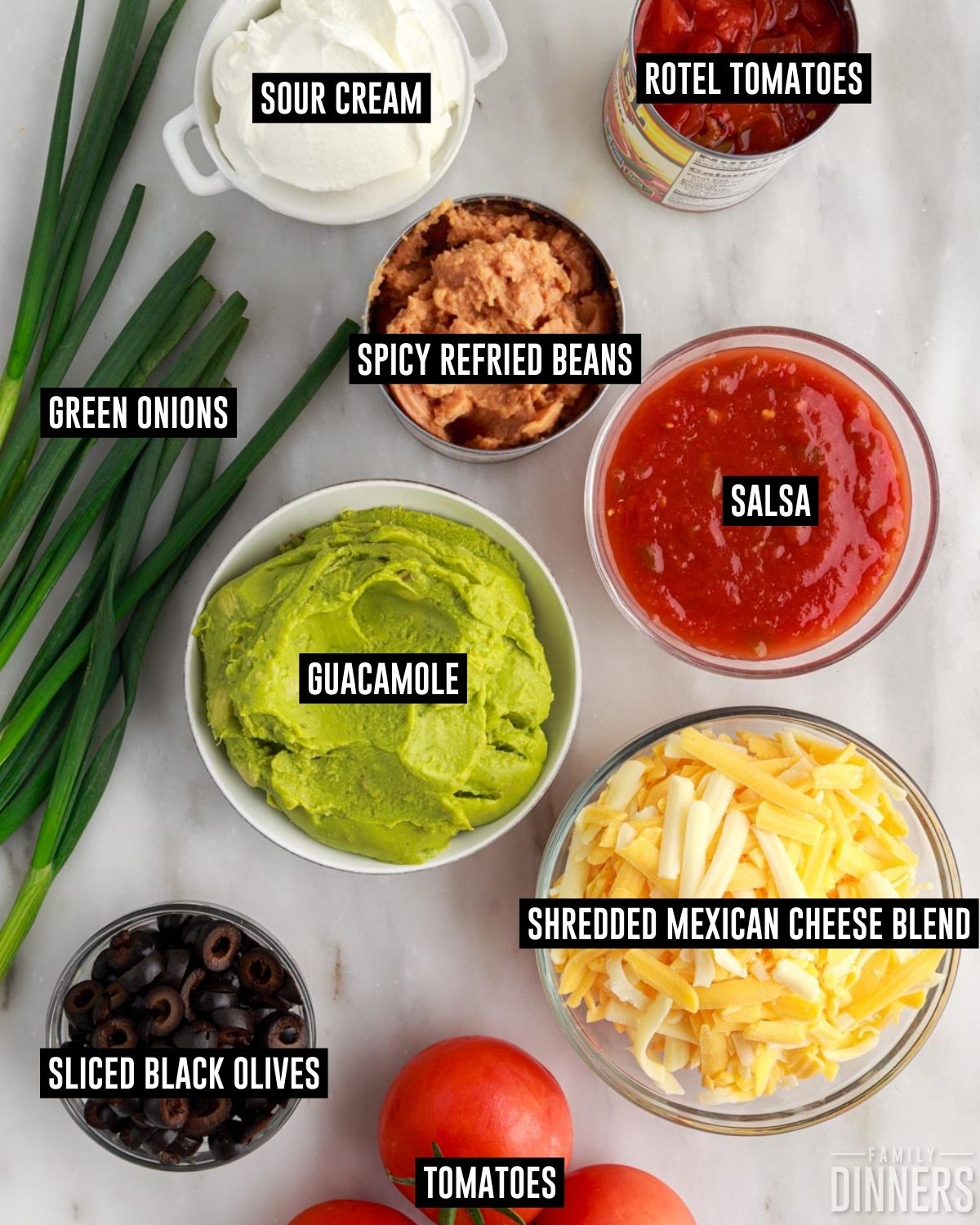 7 layer dip ingredients in containers including: shredded cheese, canned Rotel, salsa, tomatoes, sliced black olives, guacamole, spicy refried beans, sour cream, green onions.
