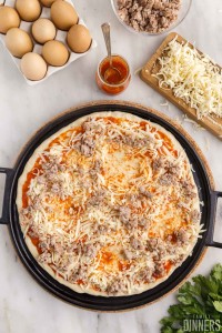 Sauce, cheese and sausage spread onto pizza crust.