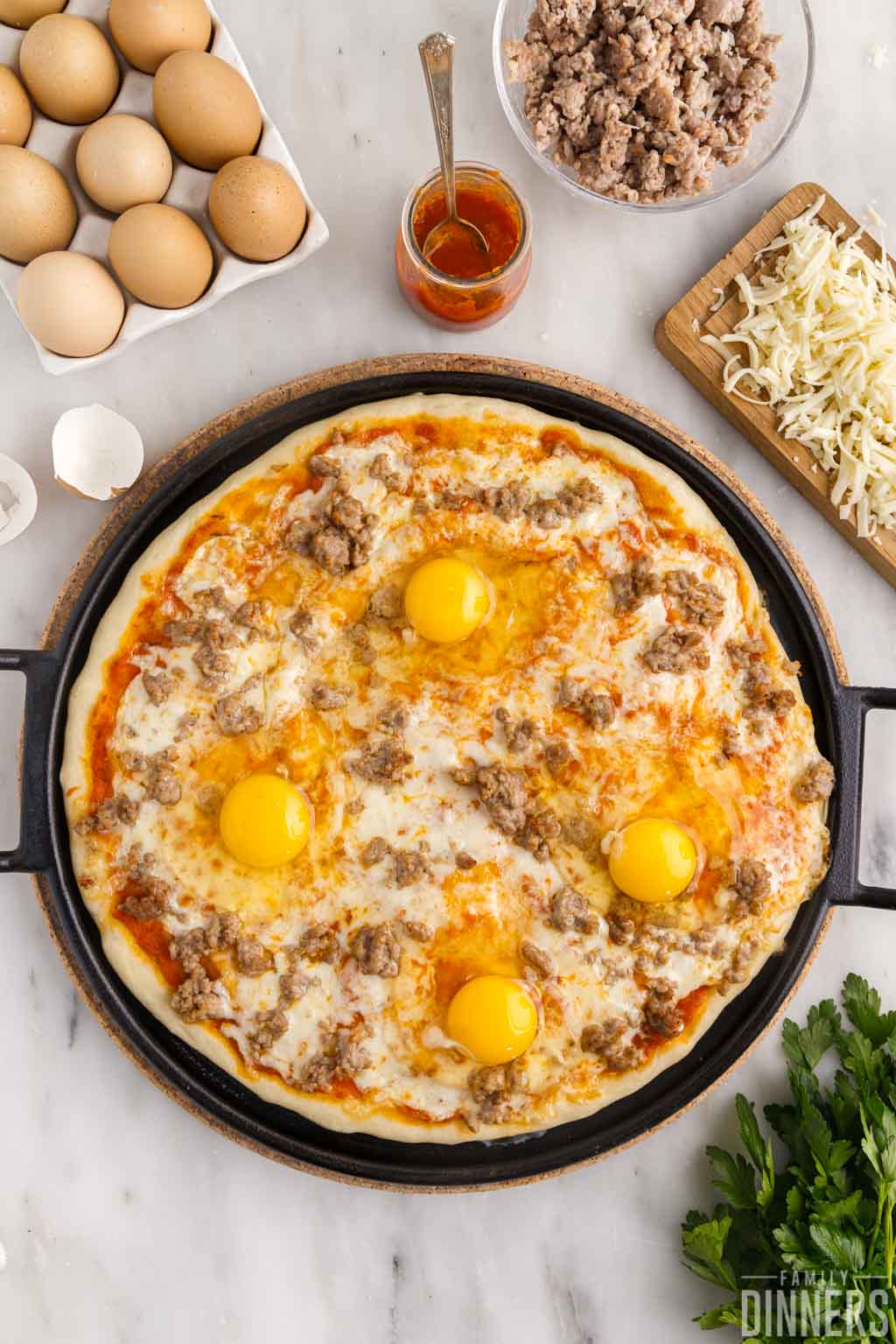 4 raw eggs on semi-cooked breakfast pizza.