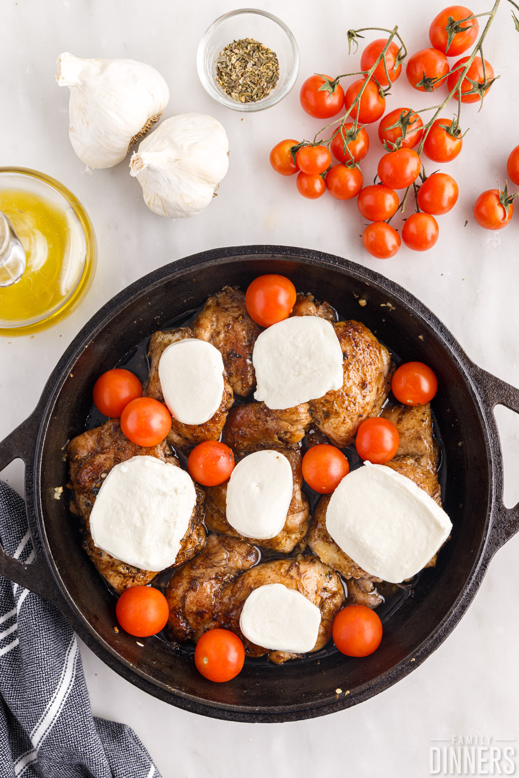 fresh mozzarella slices and raw tomatoes on chicken in a skillet.