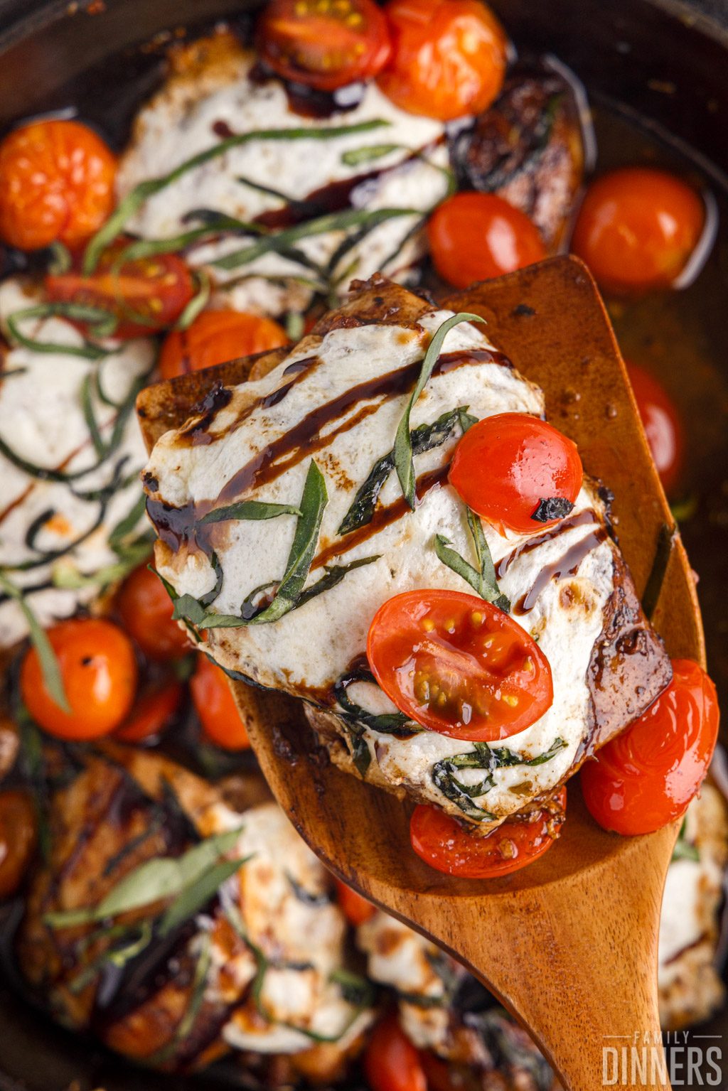 Caprese chicken with melted mozzarella and tomatoes on a spatula.