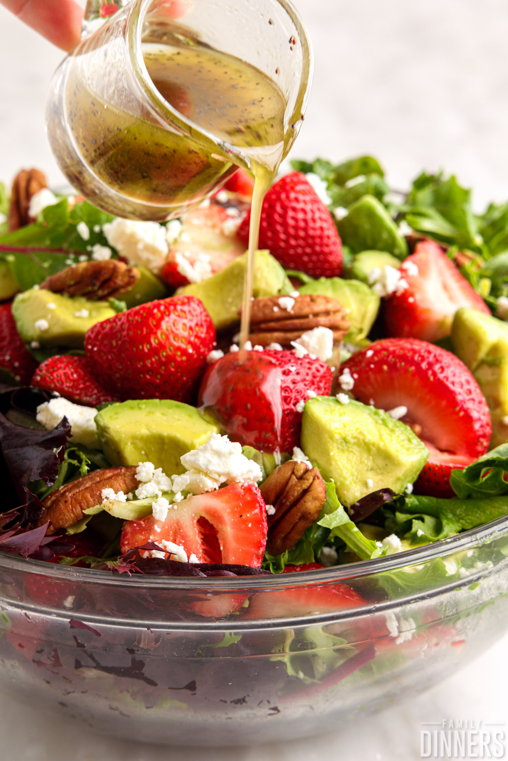 strawberry avocado salad with homemade vinaigrette pouring onto top.