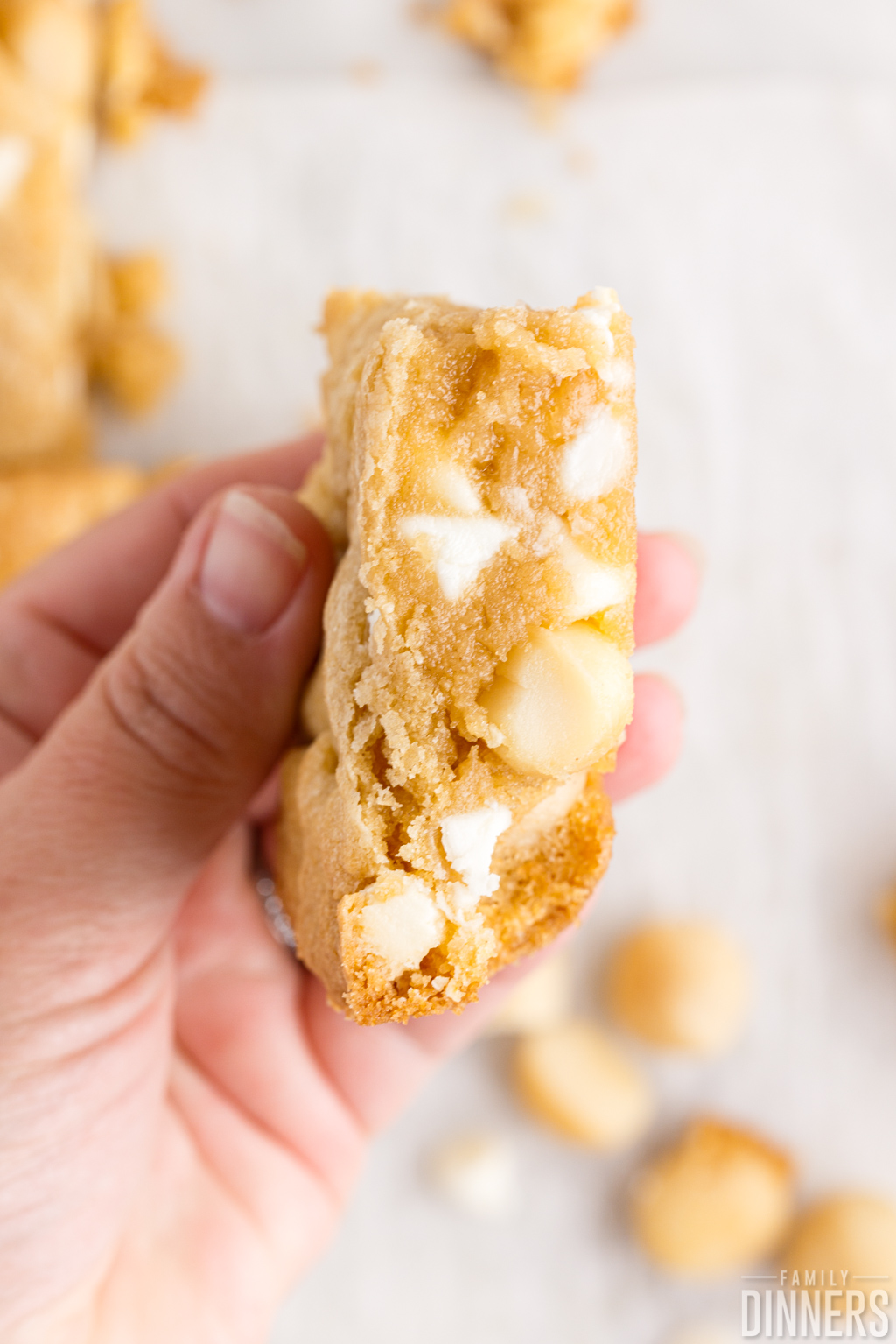 Hand holding a white chocolate macadamia nut cookie bar.