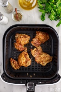 Cooked chicken thighs in an air fryer basket.