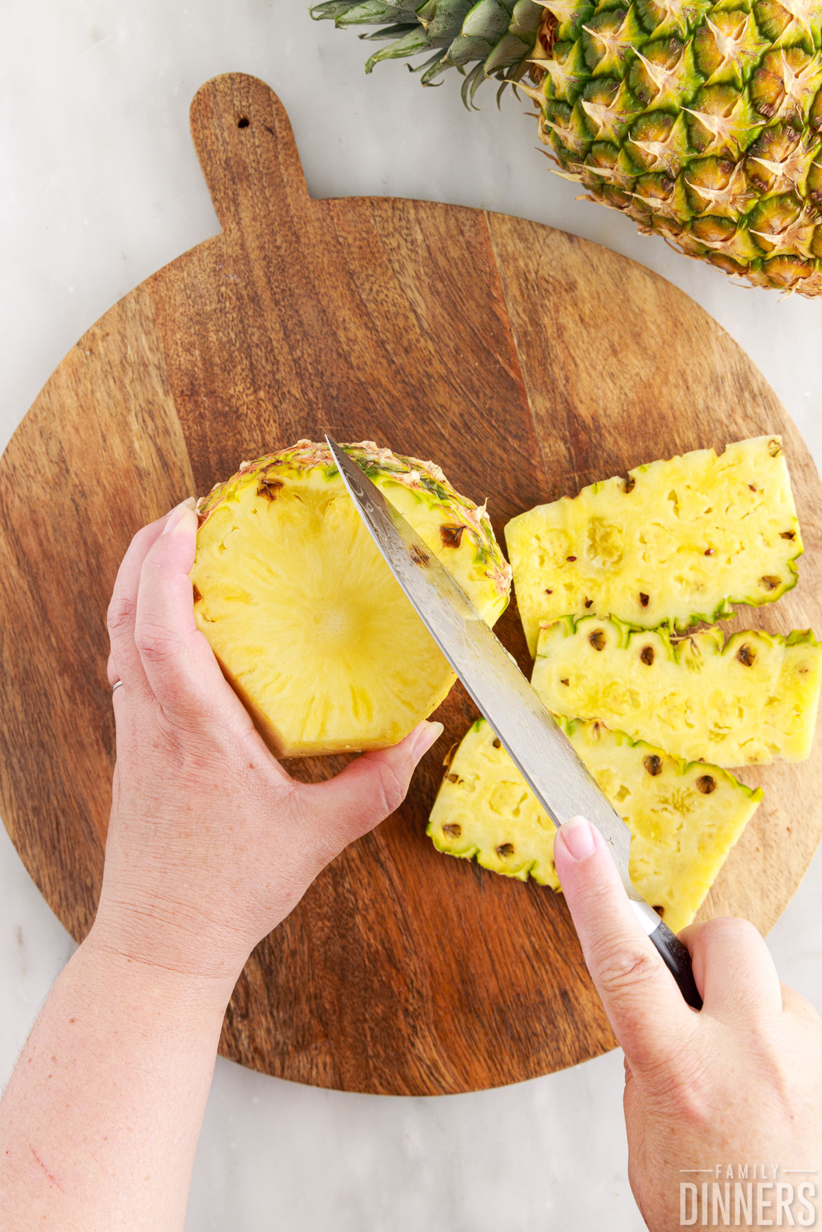 Hand cutting outside of pineapple off with a knife.