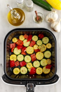 Sliced red bell pepper, zucchini and yellow squash in an air fryer basket.