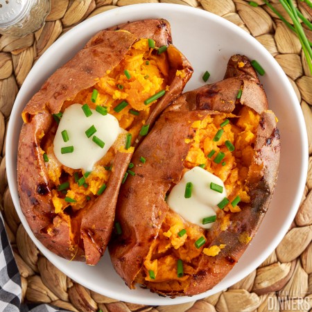 Air fryer baked sweet potatoes in a bowl with melted butter and chives.