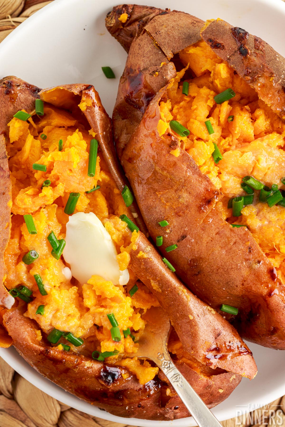 baked sweet potatoes with butter and chives on top in a bowl.
