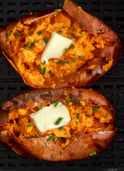 Air fryer baked sweet potatoes in an air fryer basket with melted butter and chives.