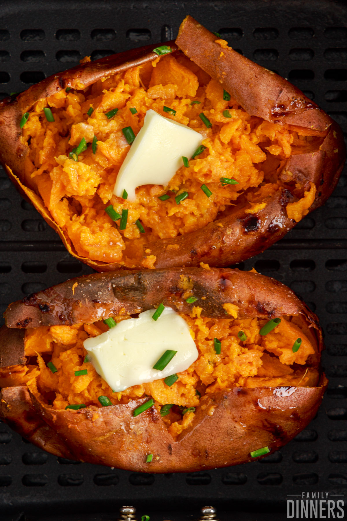 Air fryer baked sweet potatoes in an air fryer basket with melted butter and chives.