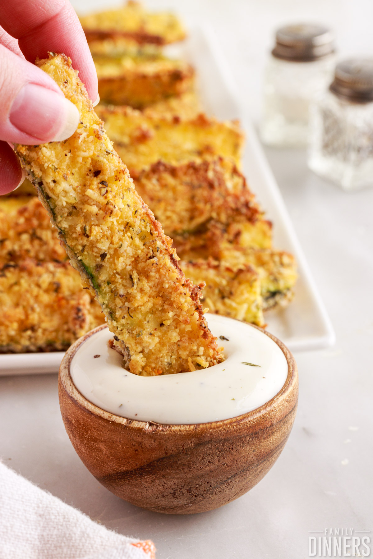 hand dipping an air fried zucchini into a dipping sauce