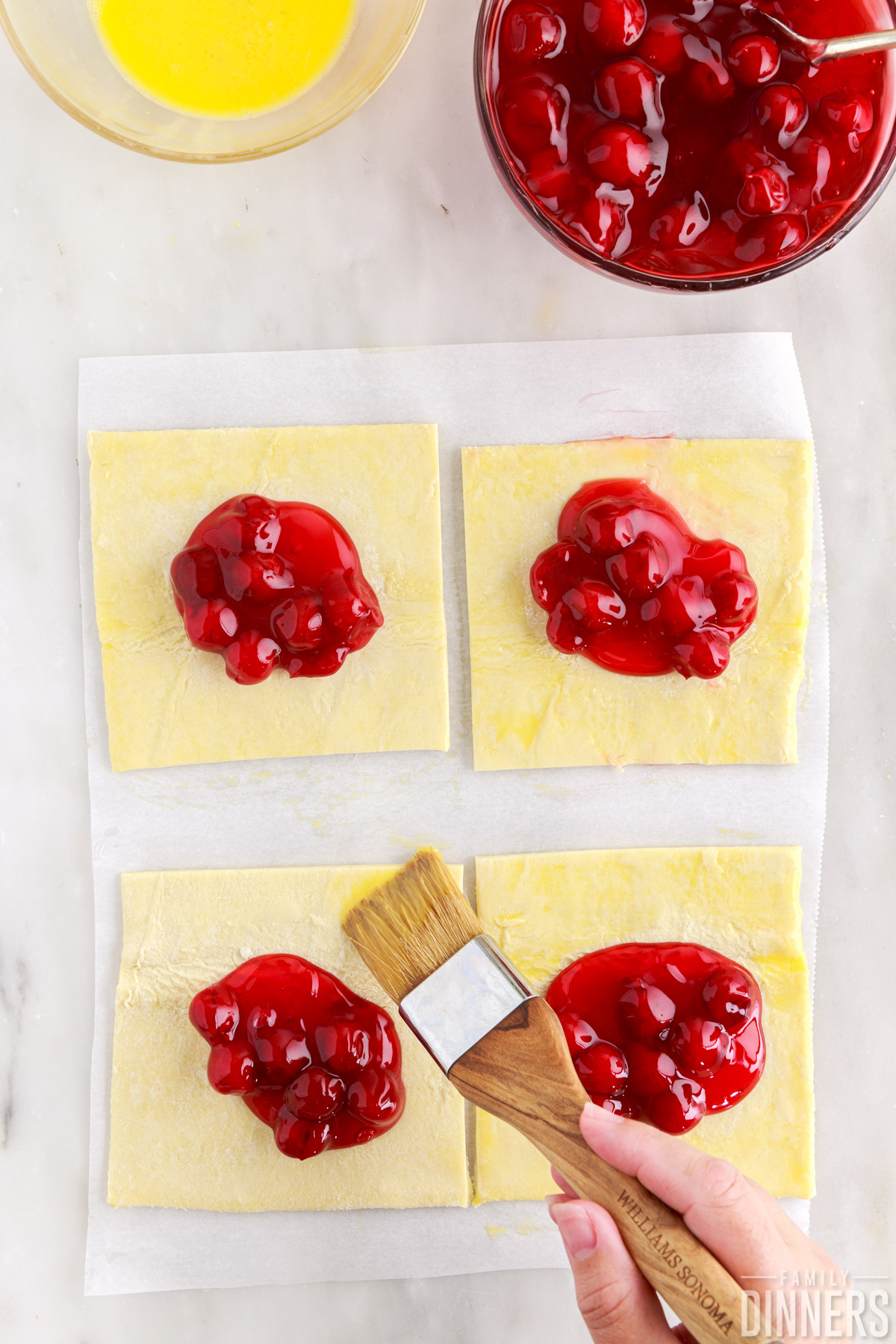 Pastry squares with cherry pie filling on top. Brush basting edges.