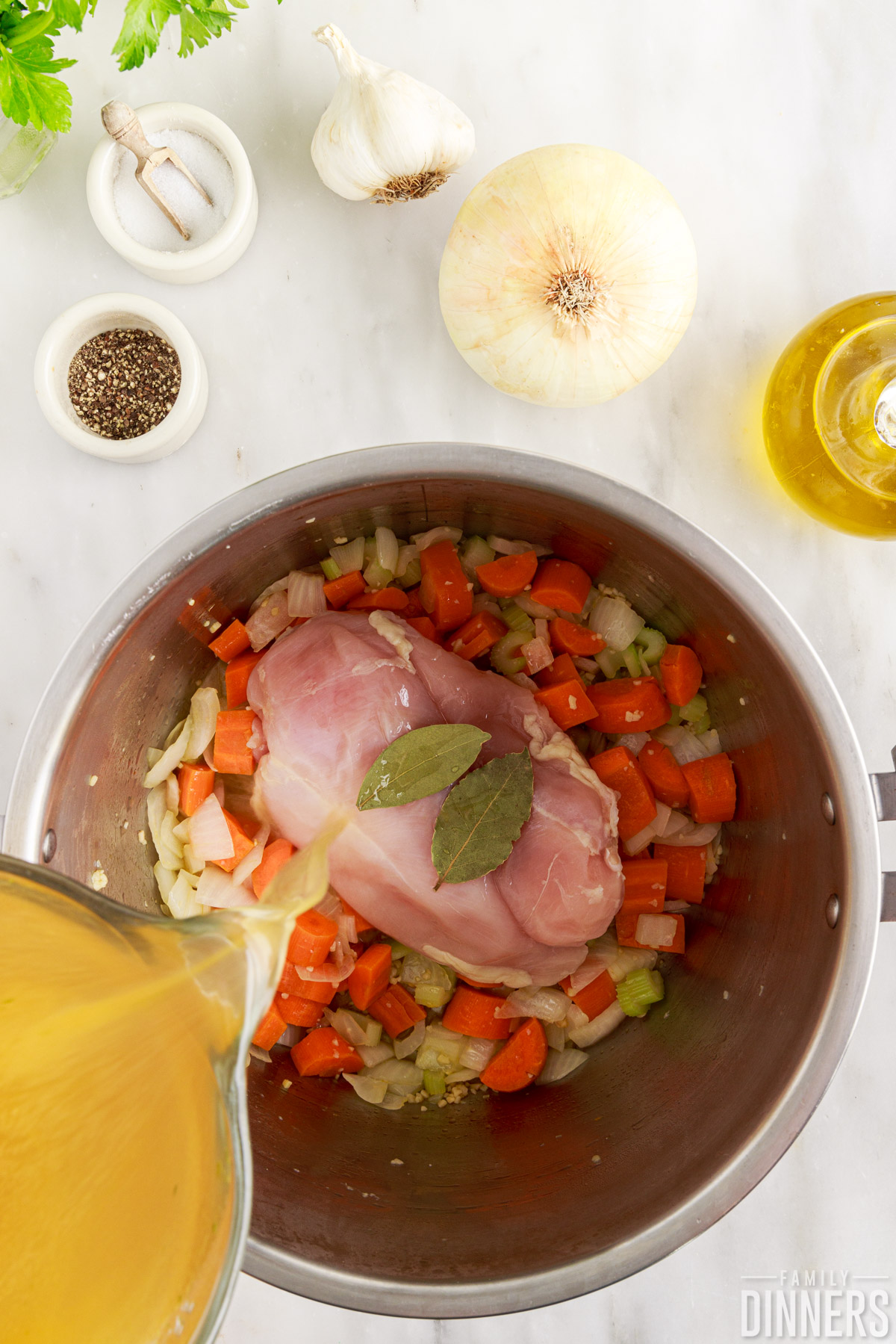 Chicken, vegetables, bay leaves in an Instant Pot while chicken broth is poured in.