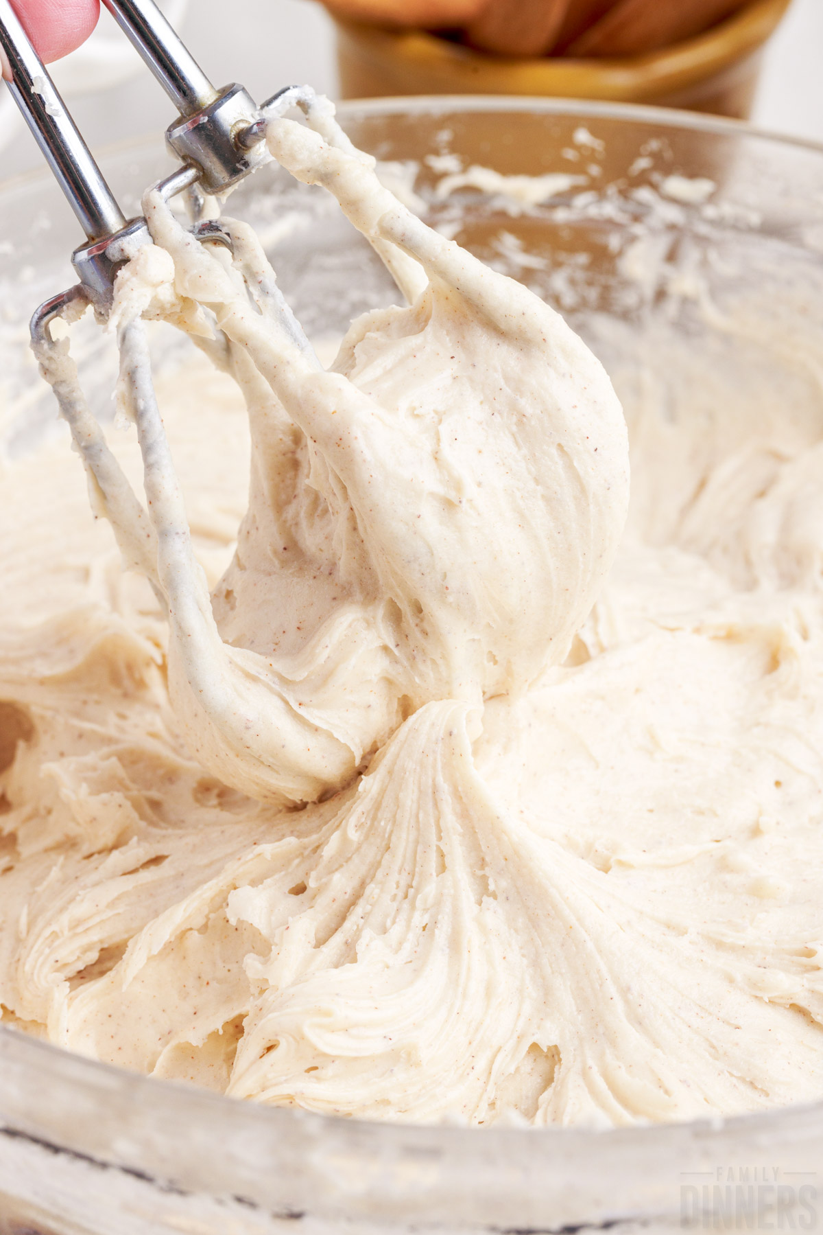 beaters covered in cinnamon frosting over a bowl of frosting