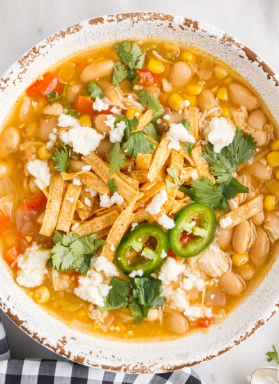 Bowl of white chicken chili with tortillas strips and cheese on top.