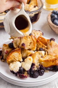 hand pouring maple syrup over French toast with blueberries