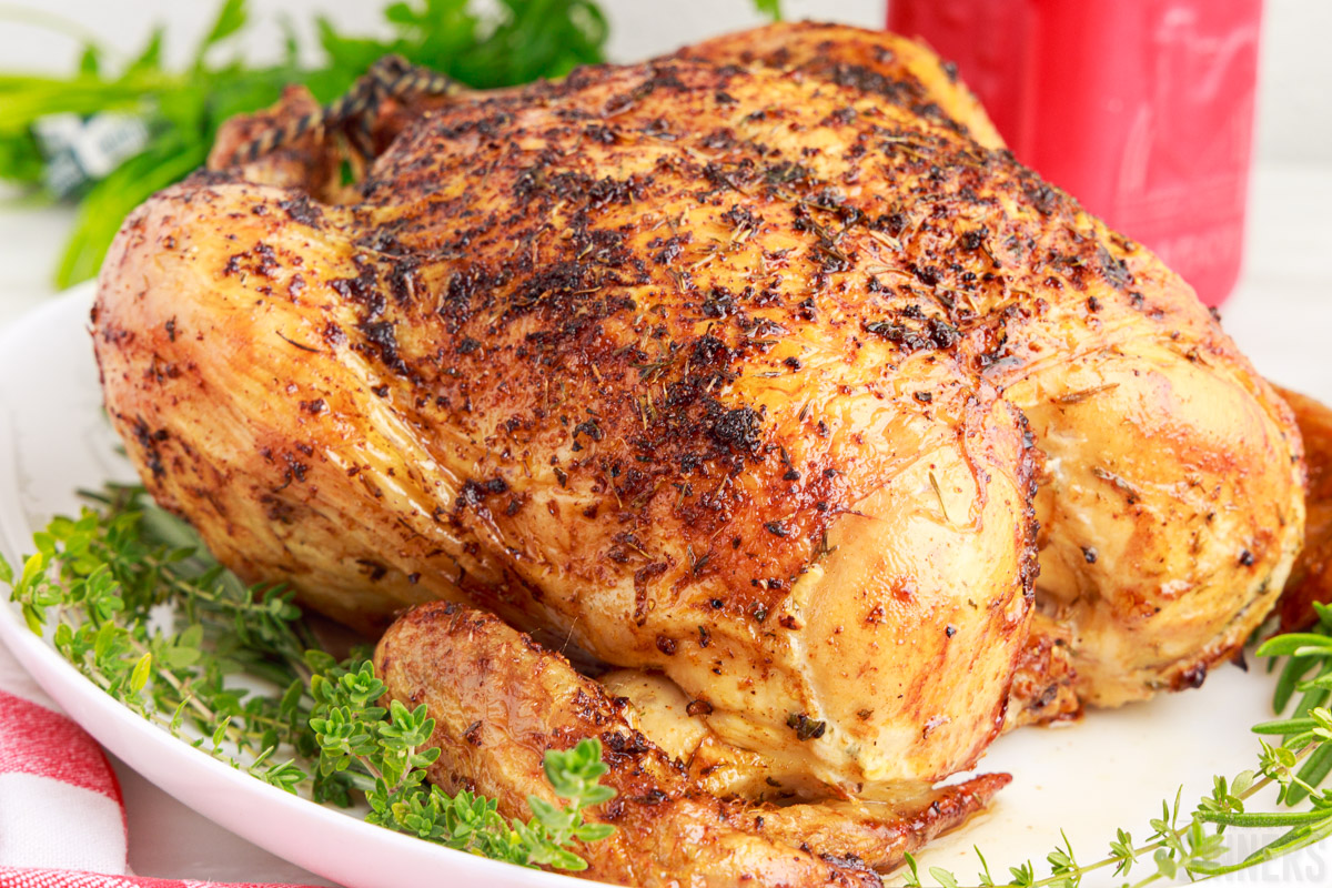 whole roasted chicken on a serving platter with fresh herbs